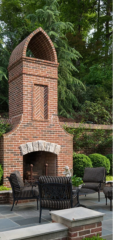 A tall brick outdoor fireplace with a herringbone chimney breast and a rough stone lintel, striped seating arranged on a bluestone terrace.